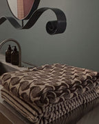 Stack of patterned towels on a bathroom counter with a sink and decorative elements in the background.